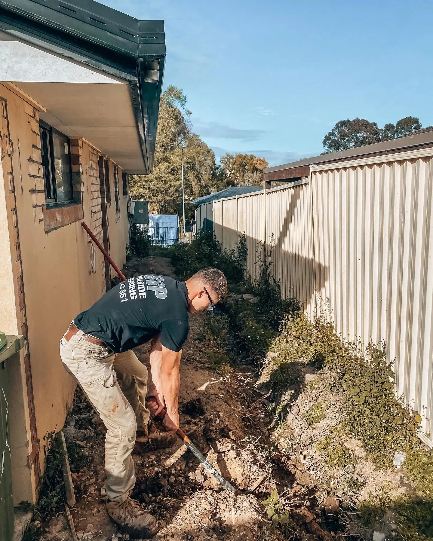 Plumber digging to expose a drain beside a house